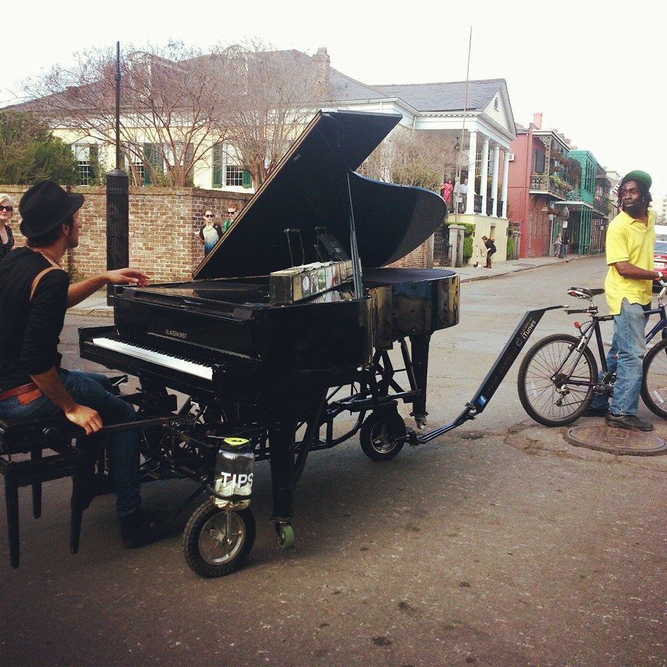 man playing piano while friend tows him on a bike